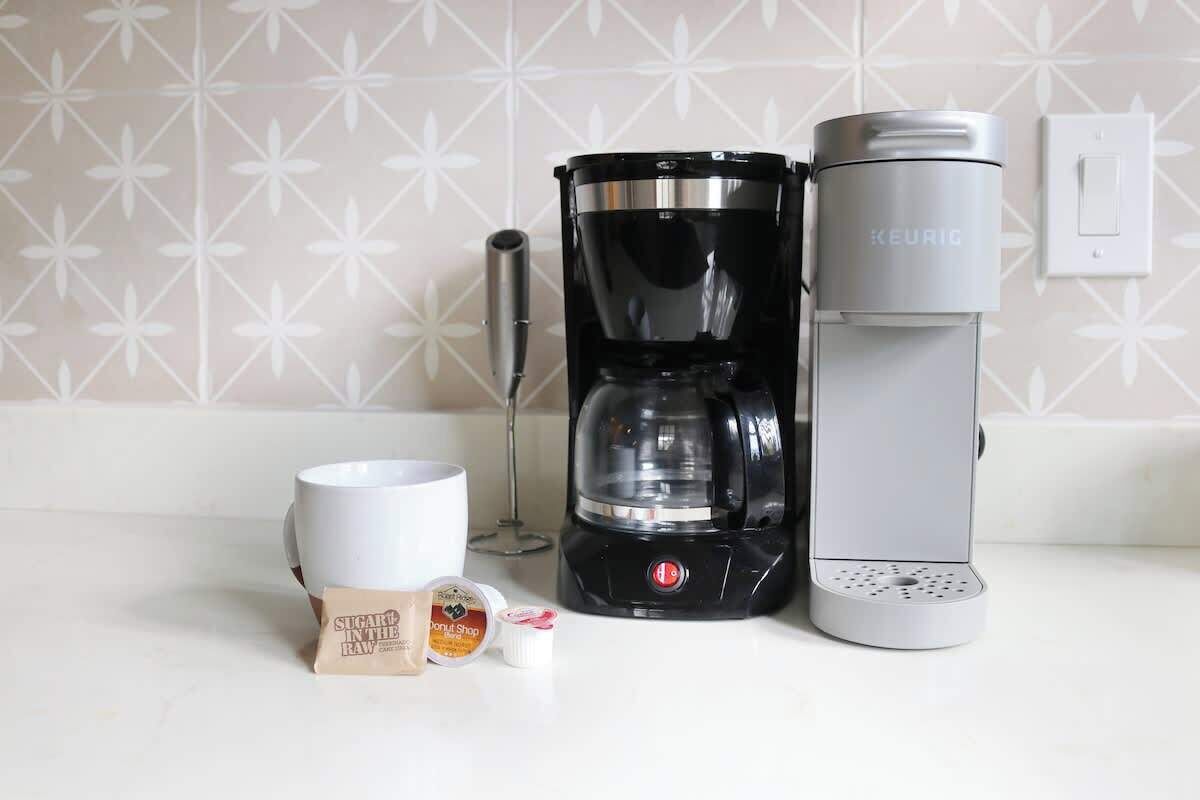 Una cafetera, una taza y un sobre de azúcar sobre una encimera de cocina.