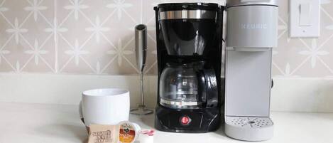 Una cafetera, una taza y un sobre de azúcar sobre una encimera de cocina.