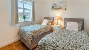 Une chambre avec deux lits, une fenêtre avec des rideaux, une table de chevet avec une lampe et un tableau au mur.