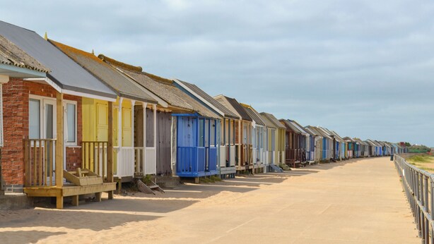Une rangée de cabanes de plage, avec un sentier sablonneux qui y mène.