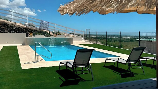 Een zwembad met een rieten parasol, twee ligstoelen en uitzicht op het landschap.