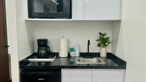 Een kleine keuken met een zwarte vaatwasser, een magnetron, een koffiezetapparaat, een spoelbak en een potplant.