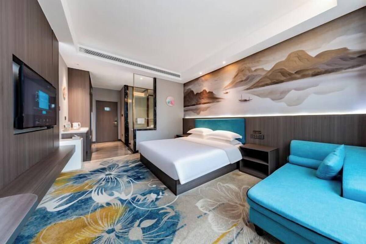 Une chambre d’hôtel moderne avec un grand lit, un canapé bleu, un téléviseur à écran plat et une fresque murale.
