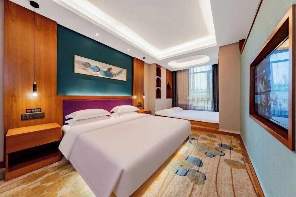 Une chambre d’hôtel avec deux lits, une grande fenêtre, un tableau au mur et une tête de lit en bois.