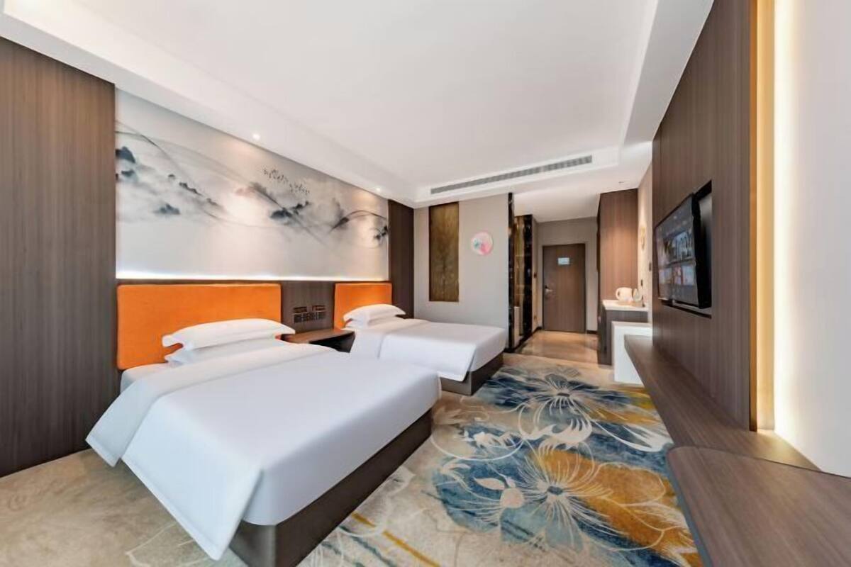 Une chambre d’hôtel avec deux lits, une grande fresque murale, une télévision et une salle de bain visible au fond.
