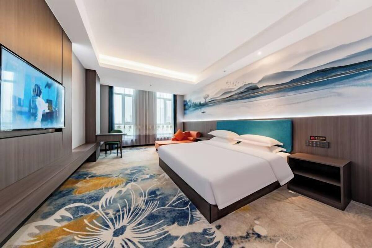 Une chambre d’hôtel moderne avec un grand lit, un bureau, une télévision et un tableau au mur.