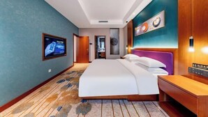 A hotel room with a bed, a TV, a wooden nightstand, and a wall-mounted light fixture.