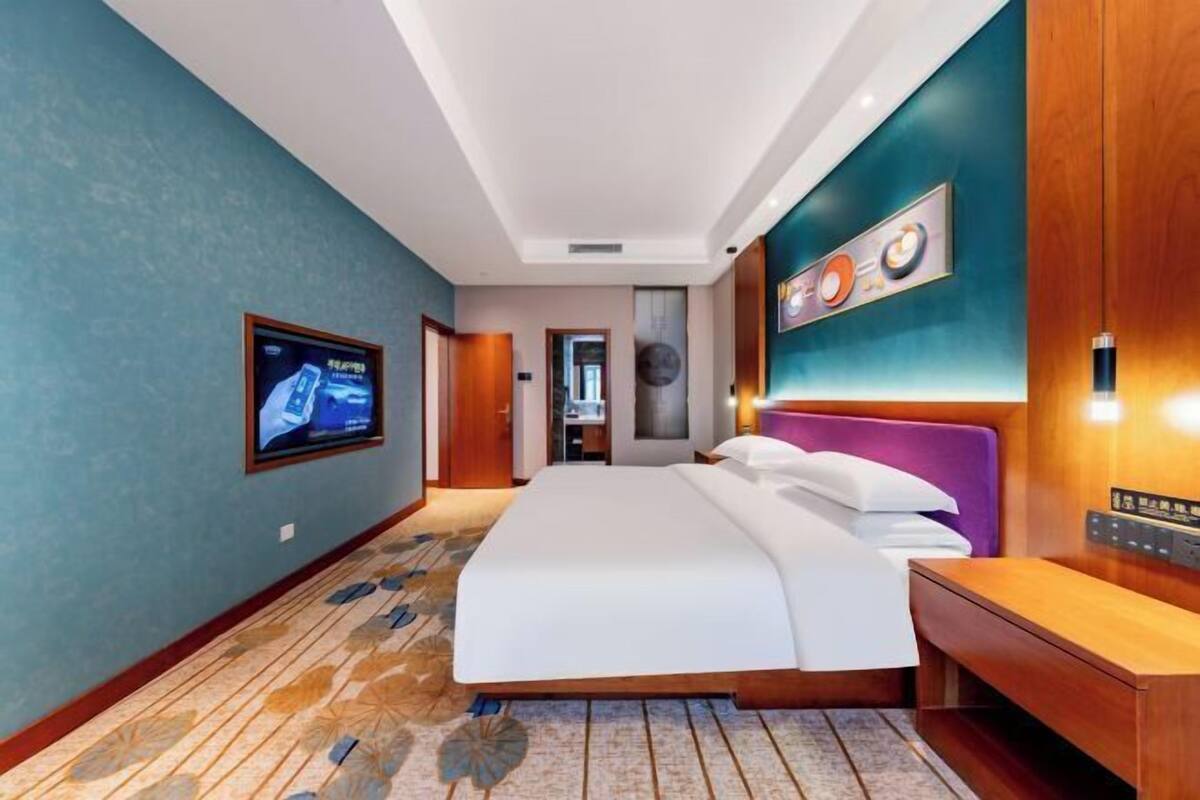 Une chambre d’hôtel équipée d’un lit, d’une télévision, d’une table de chevet en bois et d’un luminaire fixé au mur.