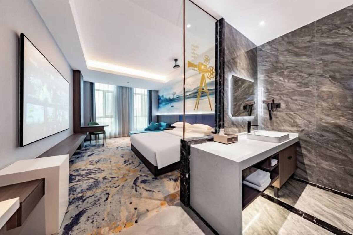 Une chambre d’hôtel moderne dotée d’un grand lit, d’une salle de bain séparée avec un meuble-lavabo en marbre et d’un grand miroir.