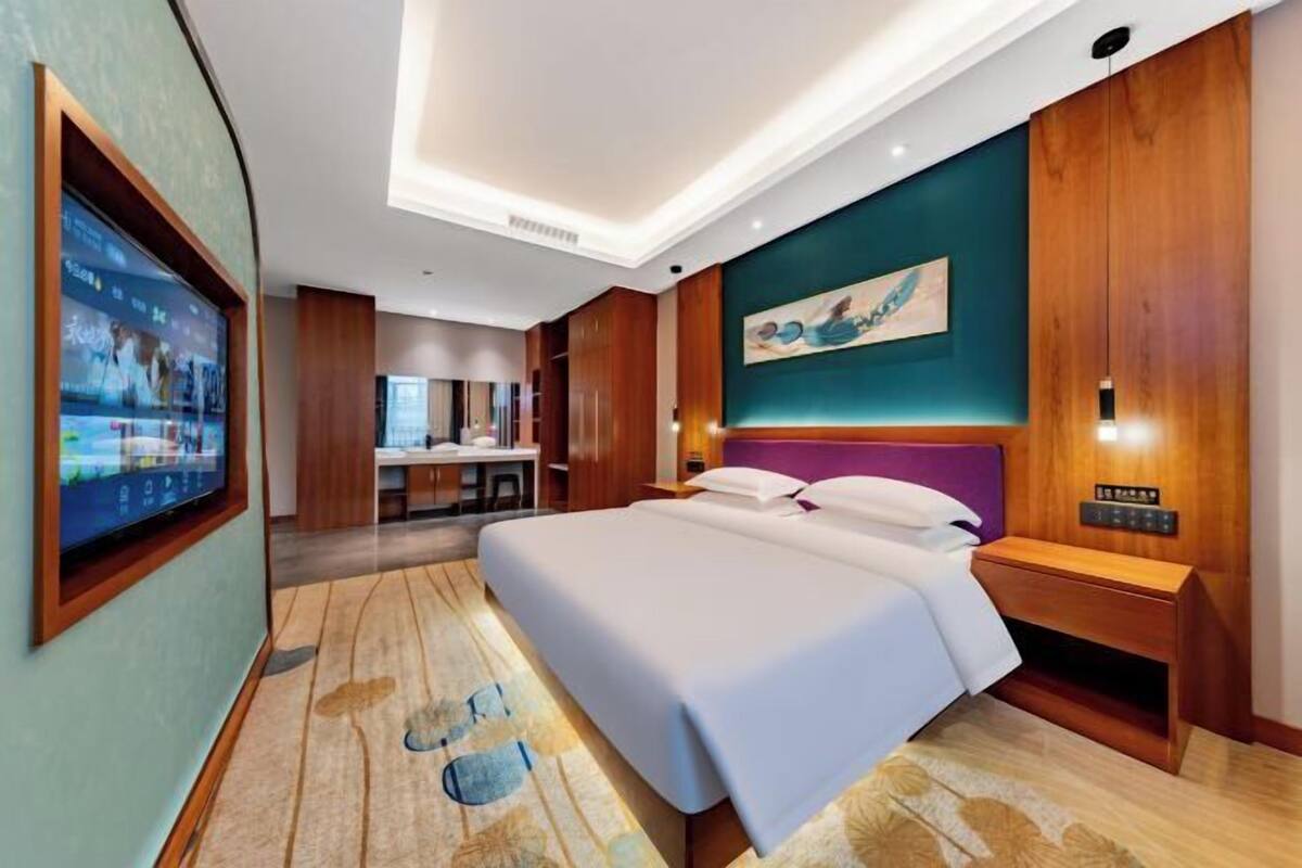 Une chambre d’hôtel moderne avec un grand lit, un bureau, une télévision et un tableau au mur.