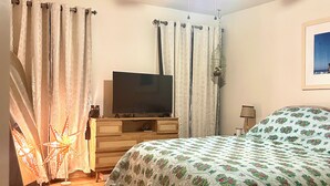 Makuuhuone, jossa on sänky, televisio puisen lipaston päällä, kattotuuletin ja verhot.