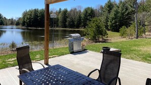 Un patio exterior con una parrilla, dos sillas y vistas a un lago.