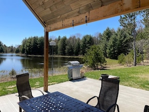 An outdoor patio with a grill, two chairs, and a view of a lake.