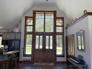 A spacious kitchen with a large wooden door, a dining area with a piano, and a view of the outdoors.
