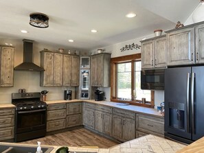 A kitchen with wooden cabinets, a black stove, a refrigerator, and a window with a view.