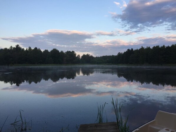 A calm lake with a dock and a boat, surrounded by dense forest.