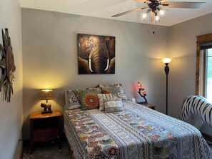 A bedroom with a bed, a ceiling fan, a wall-mounted elephant painting, a floor lamp, and a zebra-patterned chair. - Woodsy and Private- Dream House on a 7 Acre Pond (Paradise)
