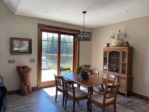 A dining area with a wooden table and chairs, a cabinet with glass doors, and a view of a lake through large sliding doors. - Woodsy and Private- Dream House on a 7 Acre Pond (Paradise)