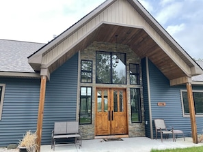 A building with a stone facade, a wooden front door, and a porch with two chairs.