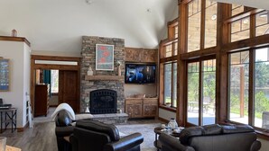 Un amplio salón con chimenea de piedra, sofás de cuero y grandes ventanales con vistas al exterior.