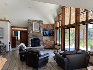 A spacious living room with a stone fireplace, leather sofas, and large windows offering a view of the outdoors.