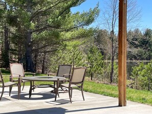 An outdoor patio with a round table and four chairs, surrounded by trees and a body of water.