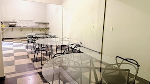 A room with a glass table and chairs, a checkered floor, and a kitchenette in the background. - Hotel Coutinho PIO XII (Pirapora)