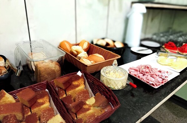 Un bufé con diversos alimentos, como pan, pasteles y fiambres.