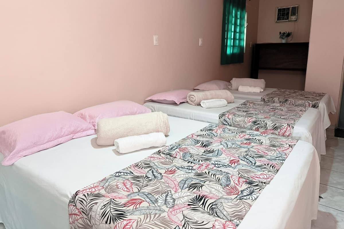 Ein Hotelzimmer mit zwei Betten, jeweils mit blumigem Überwurf, rosafarbenen Kissen und aufgerollten Handtüchern.