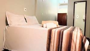 A neatly made bed with a striped blanket, a wooden wardrobe, and a door with a circular handle. - Hotel Coutinho PIO XII (Pirapora)