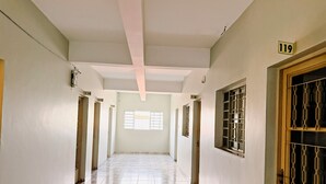 A long, narrow hallway with tiled floors and white walls. Numbered doors are visible on both sides, and a window with bars is on the right wall. - Hotel Coutinho PIO XII (Pirapora)
