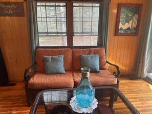 A room with a wooden paneled wall, a sofa with cushions, a wicker coffee table with a bottle, and a framed picture on the wall. - Woodsy and Private- Rustic Cabin (Paradise)