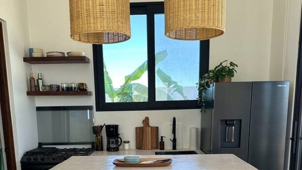 A kitchen with a central island, two wicker pendant lights, a refrigerator, and a window with a view. - Casa Cielo | Private Luxury with Ocean Views (El Pescadero)