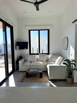 Un salon moderne avec un canapé, une table basse, un téléviseur et une grande fenêtre donnant sur un beau paysage.
