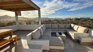 A rooftop patio with a large L-shaped sectional sofa, a wooden table, and a pergola structure. - Casa Cielo | Private Luxury with Ocean Views (El Pescadero)