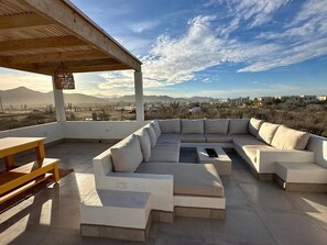 Eine Dachterrasse mit einer großen, im L-Winkel angeordneten Sitzecke, einem Holztisch und einer Pergola.