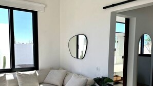 A modern living room with a sectional sofa, a coffee table, a potted plant, and a wall-mounted mirror. - Casa Cielo | Private Luxury with Ocean Views (El Pescadero)