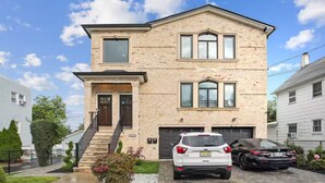 A two-story brick house with a front porch, a garage, and two cars parked in the driveway. - Saddle Ridge at Kearny - Luxury 4-Bedroom Oasis (Kearny)