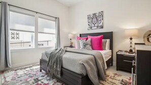 A bedroom with a bed, a nightstand, a lamp, a window with curtains, and a wall-mounted artwork. - Saddle Ridge at Kearny - Luxury 4-Bedroom Oasis (Kearny)