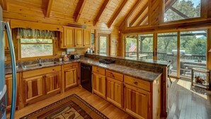 A wooden cabin kitchen with a large island, wooden cabinets, and a view of the outdoors. - Bearway to Heaven Lake View Fire Pit Game Room (Blue Ridge)
