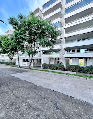 A multi-story building with balconies, a parking lot, and a street with trees. - Lindo estudio a pasos del Metro Los Dominicos (Santiago)