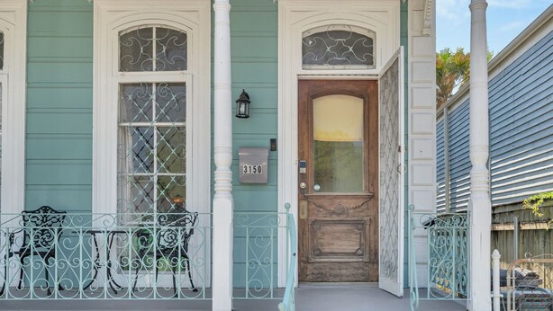 A teal house with white trim, a wooden front door, and a mailbox.