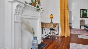 A room with a white fireplace, a wooden desk, a chair, a vase with dried plants, and a yellow curtain.
