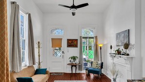A room with a sofa, a chair, a table with a plant, a fireplace, and a ceiling fan.
