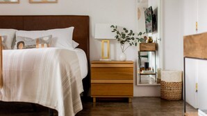 A neatly arranged bedroom with a bed, bedside table, lamp, and a mirror.