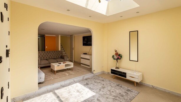 A modern living room with a sofa, coffee table, and a TV. There's a skylight above and a mirror on the wall. - Family house in the north of Bogota (Bogotá, D.C.)