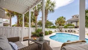 En täckt uteplats med möbler i rotting, en pool och palmer.