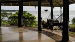 Un espace extérieur abrité, doté d’un hamac et d’un panier suspendu, qui offre une vue sur une étendue d’eau et la verdure environnante.