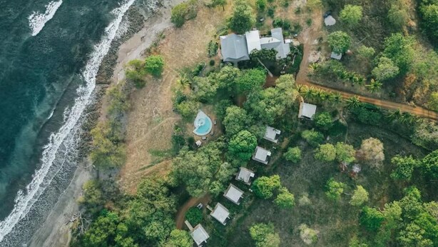 Vue aérienne d’une propriété située sur la côte, comprenant plusieurs maisons, une piscine et une plage.