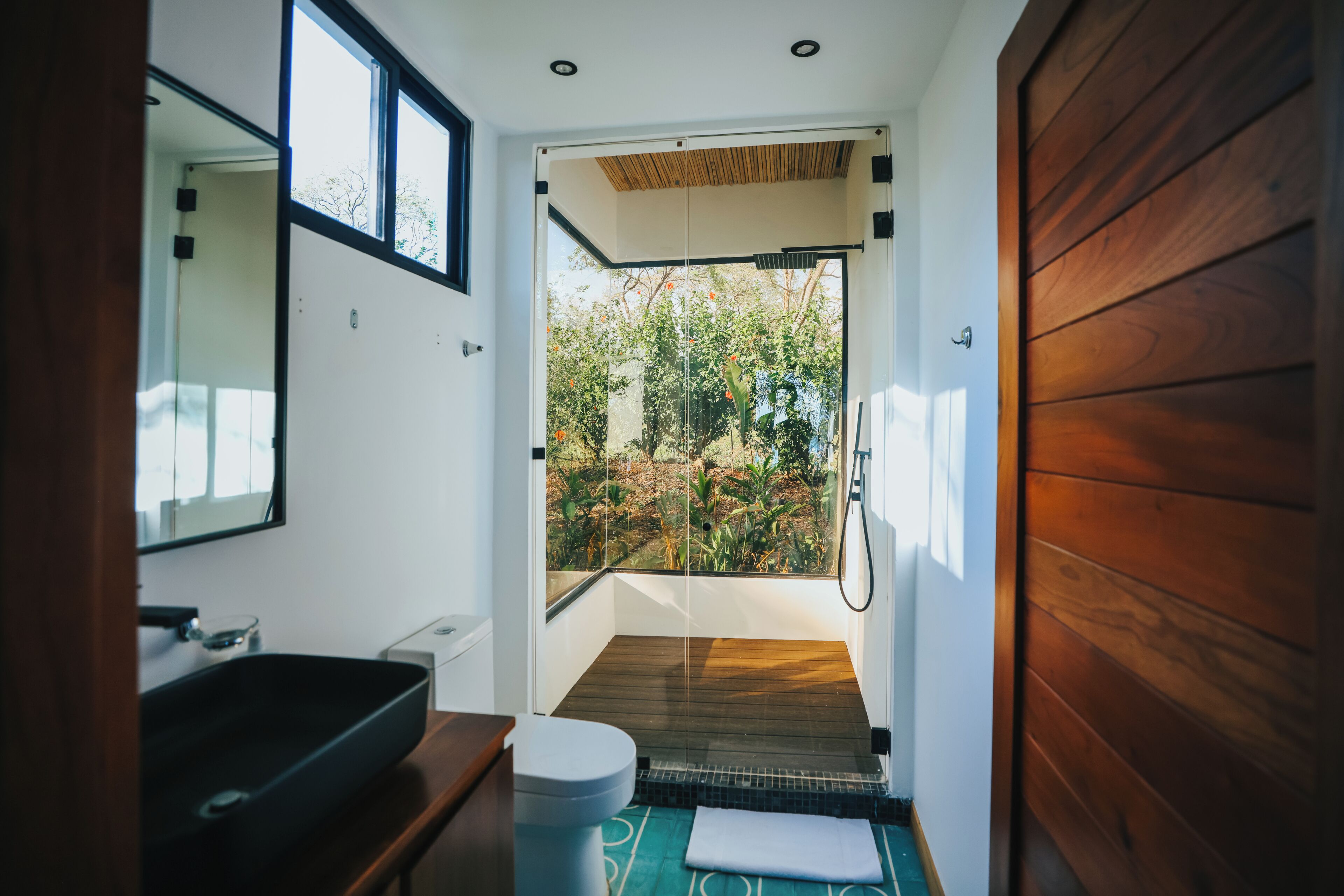 A modern bathroom with a large window, a wooden door, and a sink.
